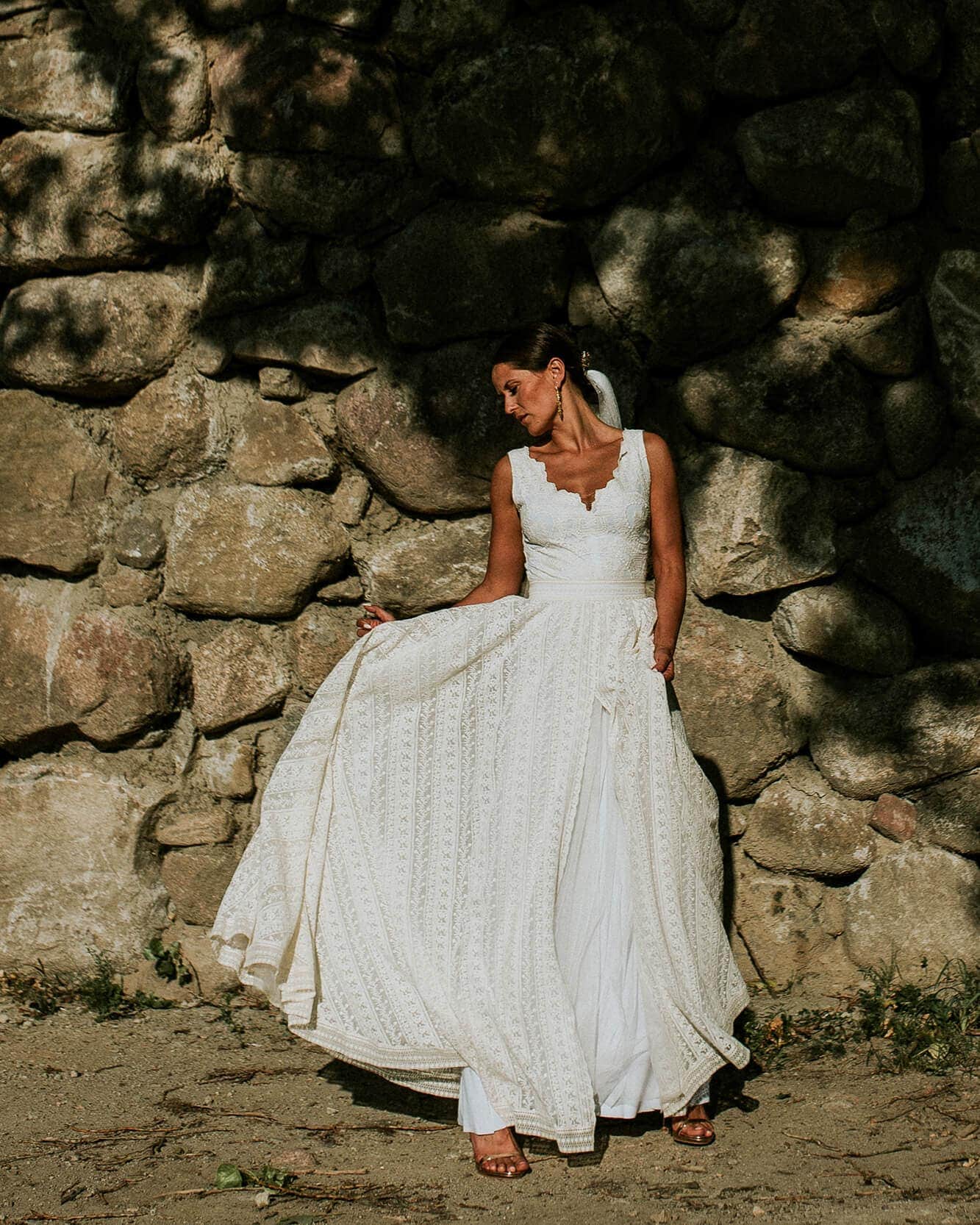 suknia ślubna z dekoltem w serek, stojąca na tle kamiennej ściany