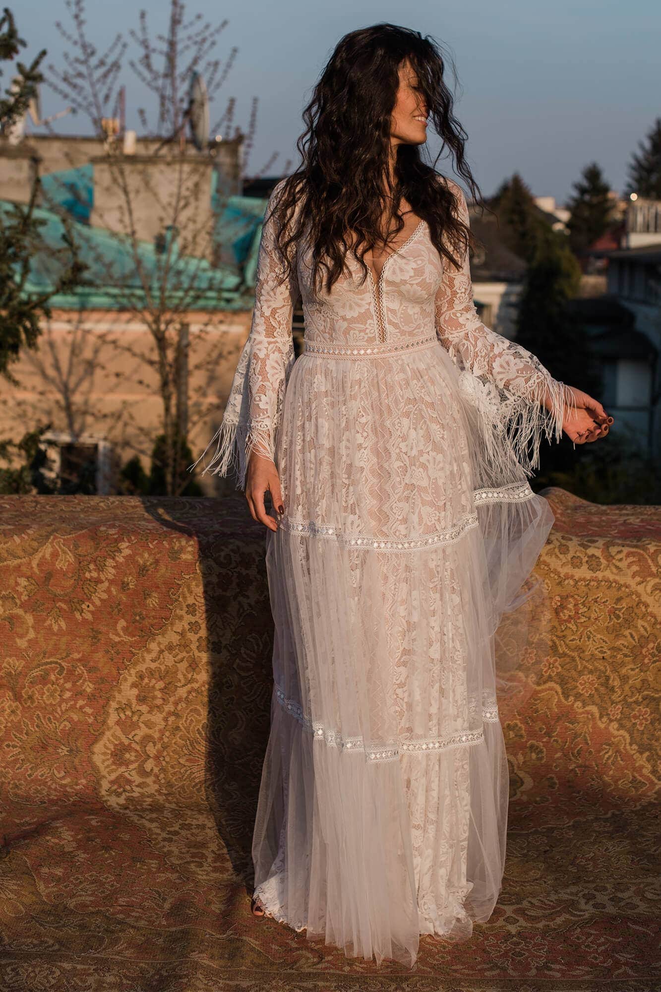 suknia ślubna z długimi rękawami i koronkowymi detalami, noszona przez kobietę na tle krajobrazu.