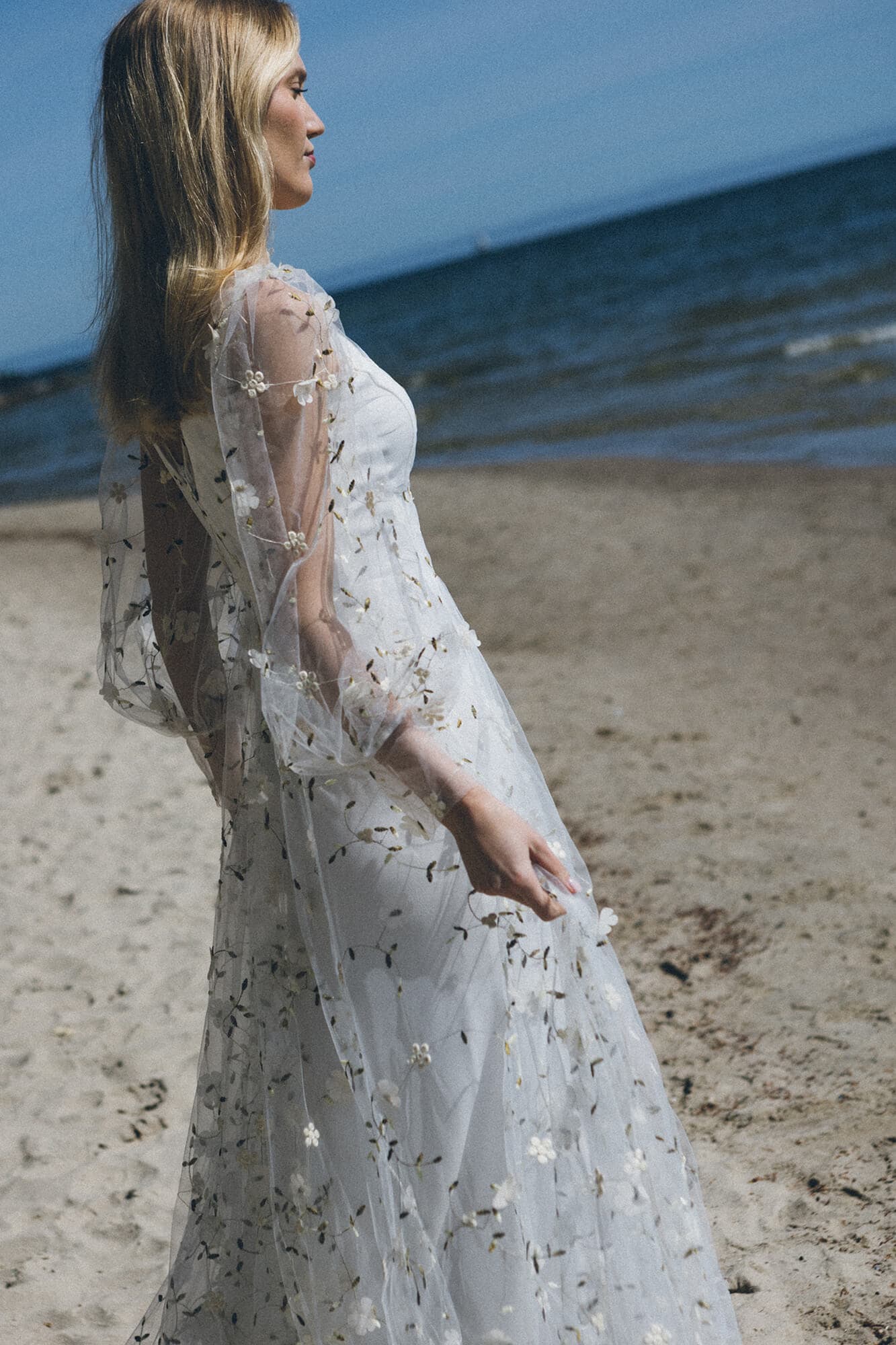 suknia ślubna z długimi rękawami i koronkowymi detalami, na tle plaży i morza