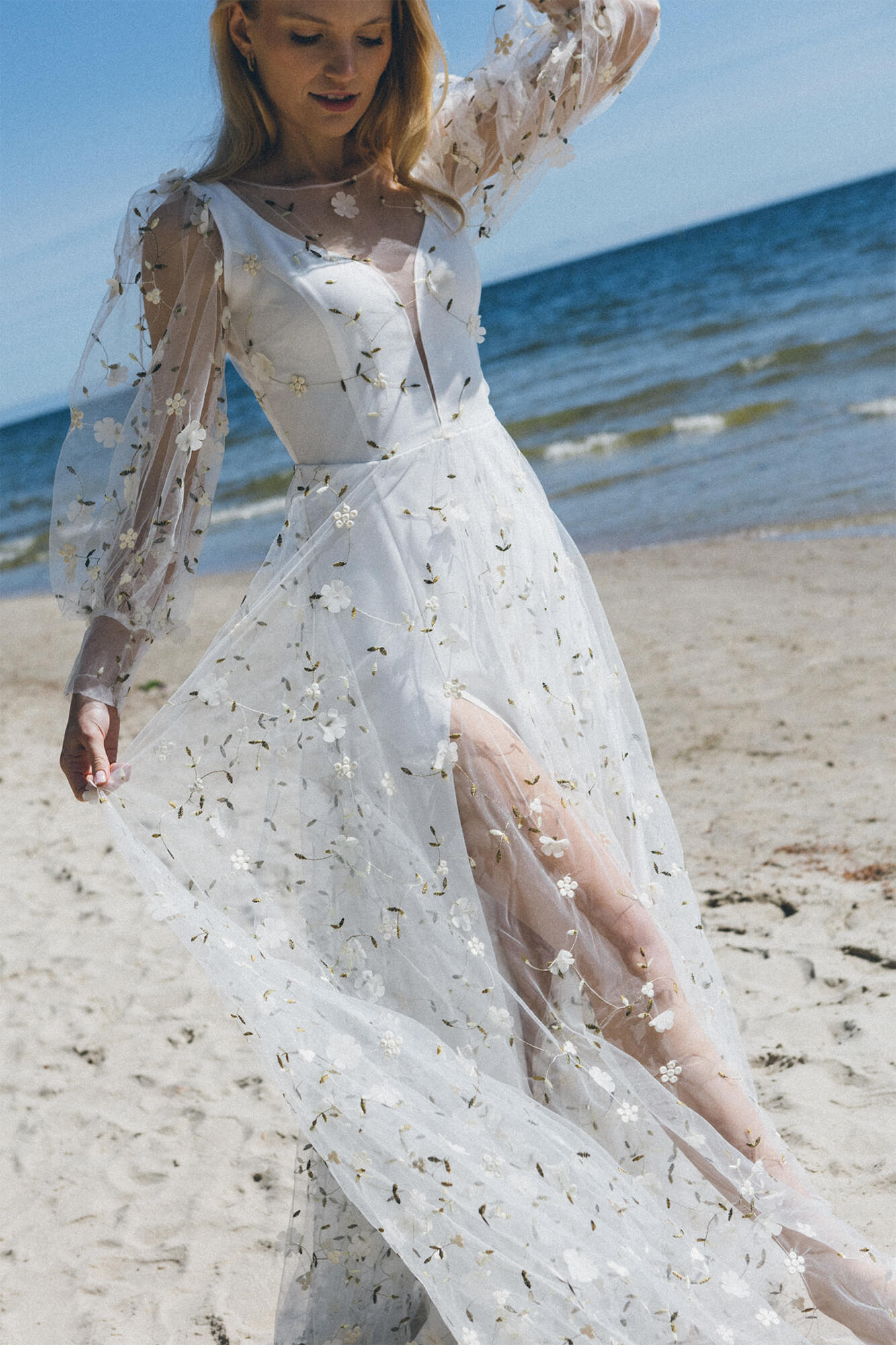suknia ślubna z długimi rękawami, ozdobiona kwiatowymi aplikacjami, na plaży w nadmorskim otoczeniu