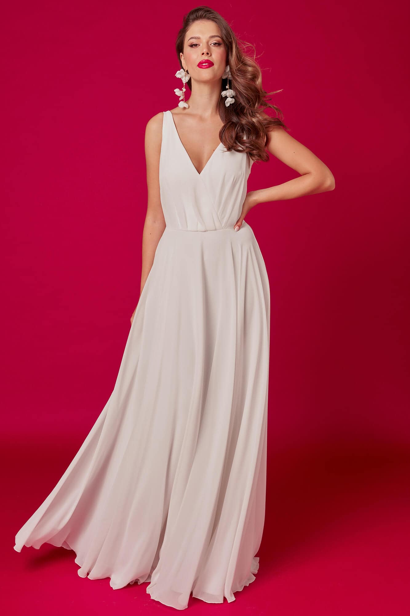 suknia ślubna o prostym kroju, z dekoltem w kształcie litery V, na tle różowej ściany