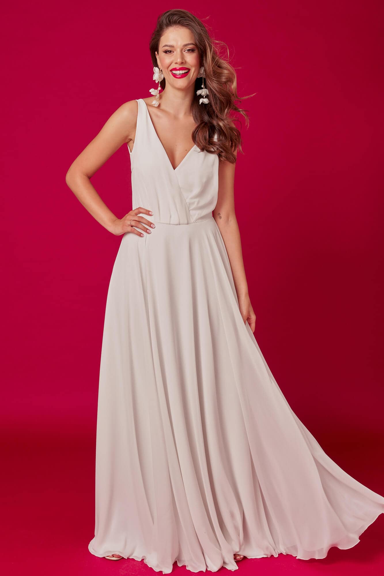 suknia w jasnym kolorze z dekoltem w kształcie litery V i luźnym dołem, modelka stoi na tle różowej ściany