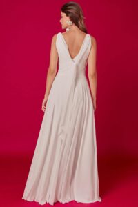 suknia ślubna z długim, zwiewnym dołem i dekoltem w serek z tyłu, na tle różowej ściany