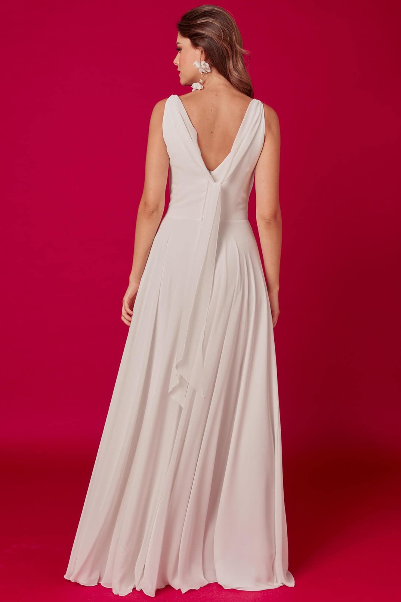 suknia ślubna z długim, zwiewnym dołem i dekoltem w serek z tyłu, na tle różowej ściany