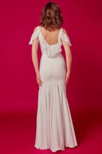 suknia ślubna z odkrytymi ramionami i falbanami, widok z tyłu, na tle różowej ściany
