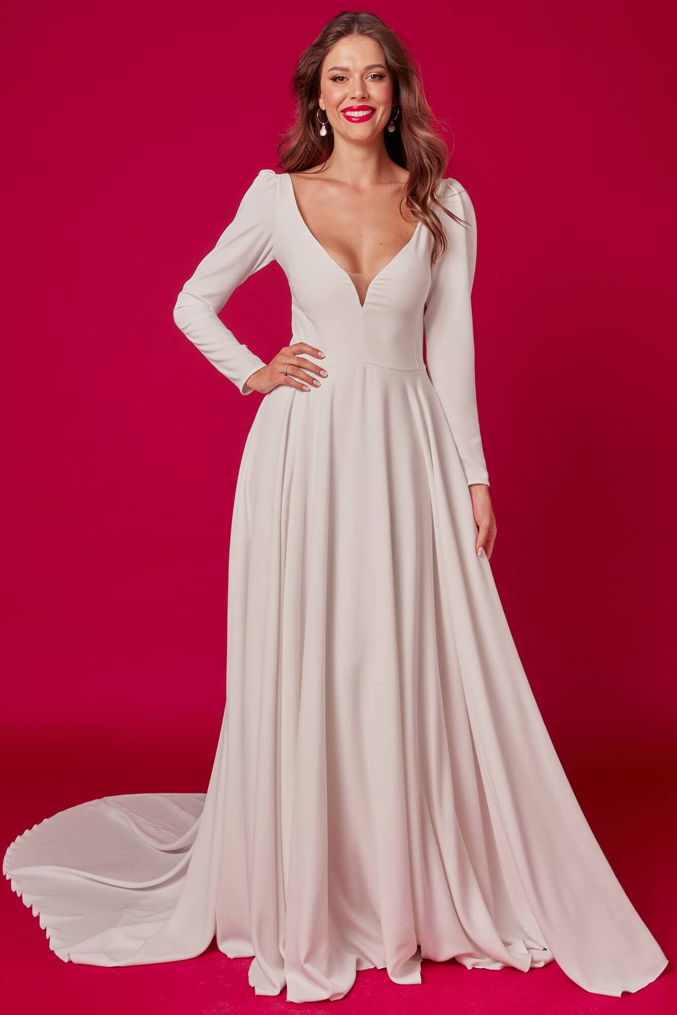 suknia ślubna o długich rękawach i głębokim dekolcie, z trenem na tle różowego tła