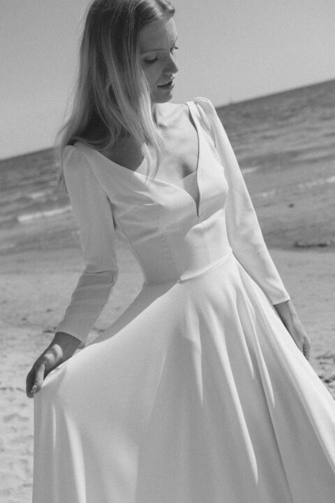 suknia ślubna z długimi rękawami, dekoltem w serek i rozkloszowanym dołem, na tle plaży