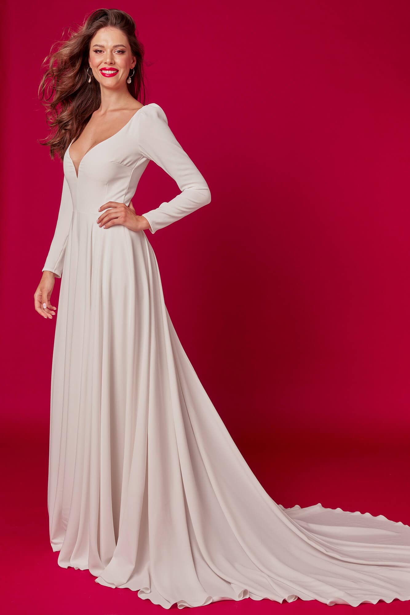 suknia ślubna o długim rękawie, z dekoltem w serek i długim trenem, na tle czerwonego tła
