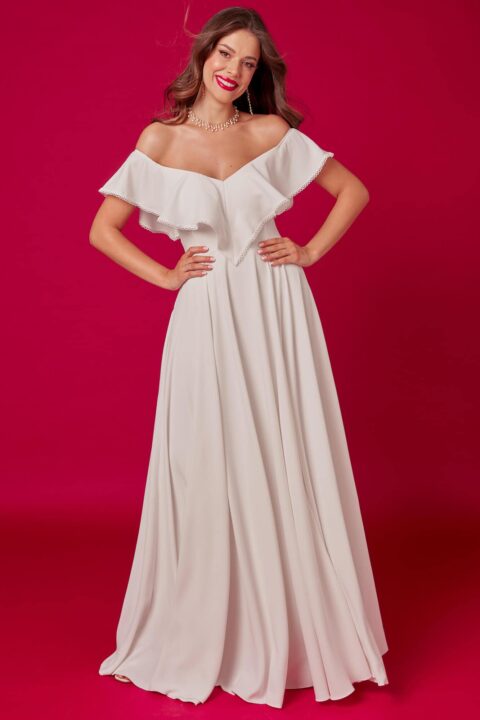 suknia ślubna z odkrytymi ramionami i falbaną, w kolorze białym, na tle różowej ściany