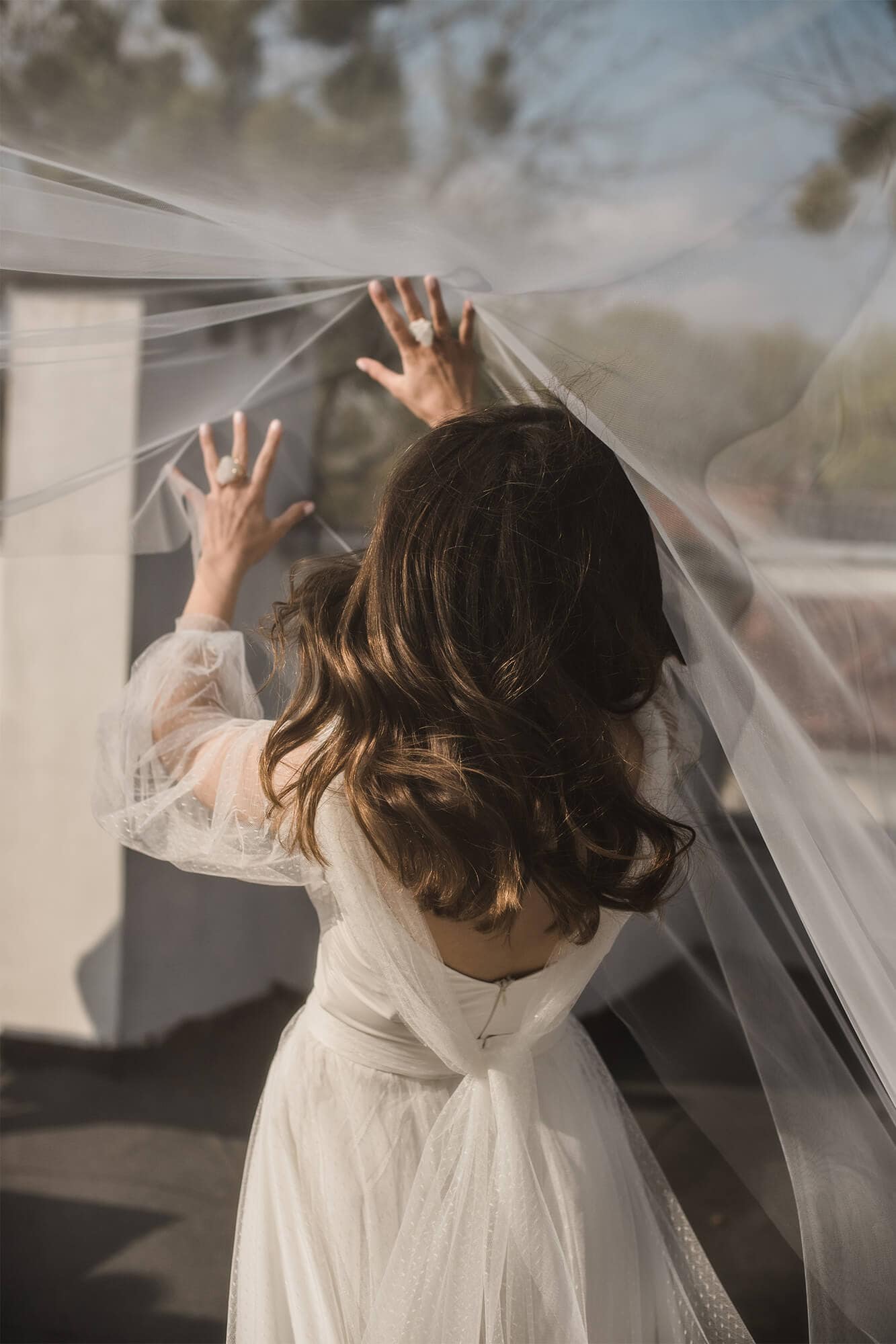 Kobieta w sukni ślubnej z długimi rękawami trzyma woal.