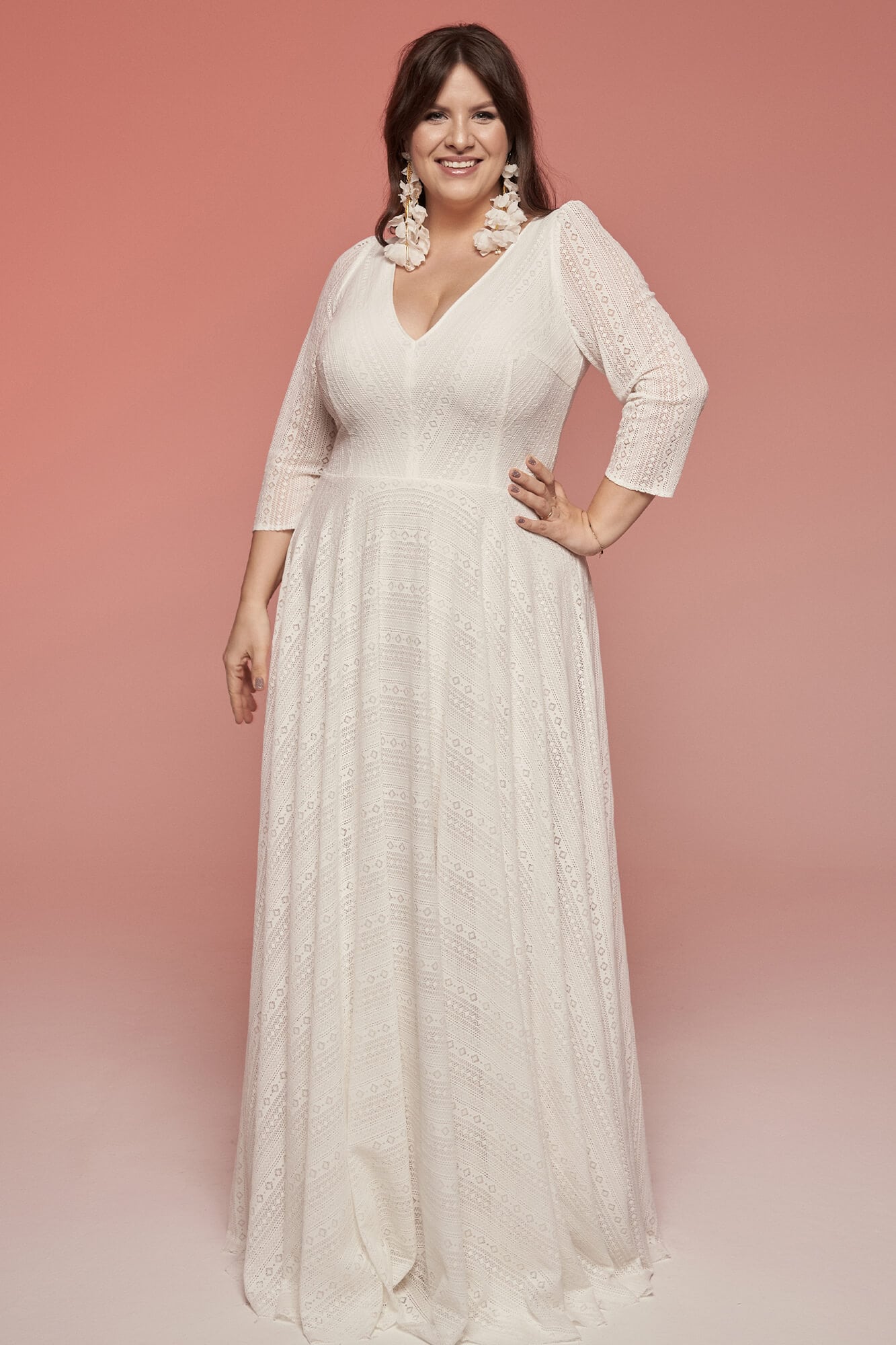 suknia ślubna z długim rękawem i dekoltem w serek, w kolorze białym, z falbanami na dole.