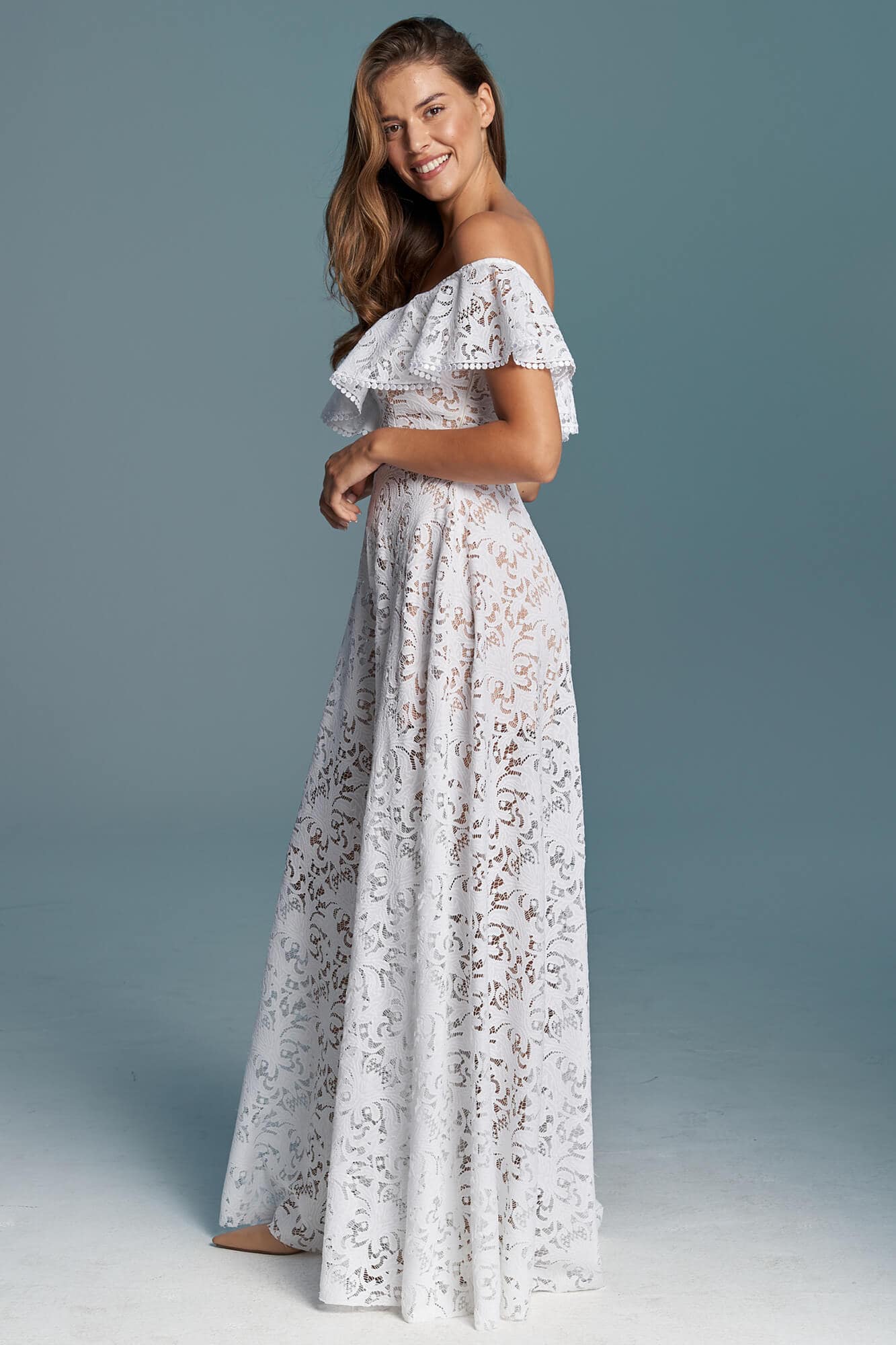 suknia w kolorze białym z koronkowym wzorem i odkrytymi ramionami, modelowana na sylwetce kobiecej