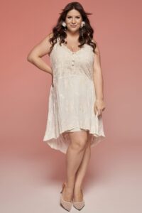 suknia w kolorze jasnoróżowym z koronkowymi detalami i asymetrycznym dołem, na modelce z długimi włosami