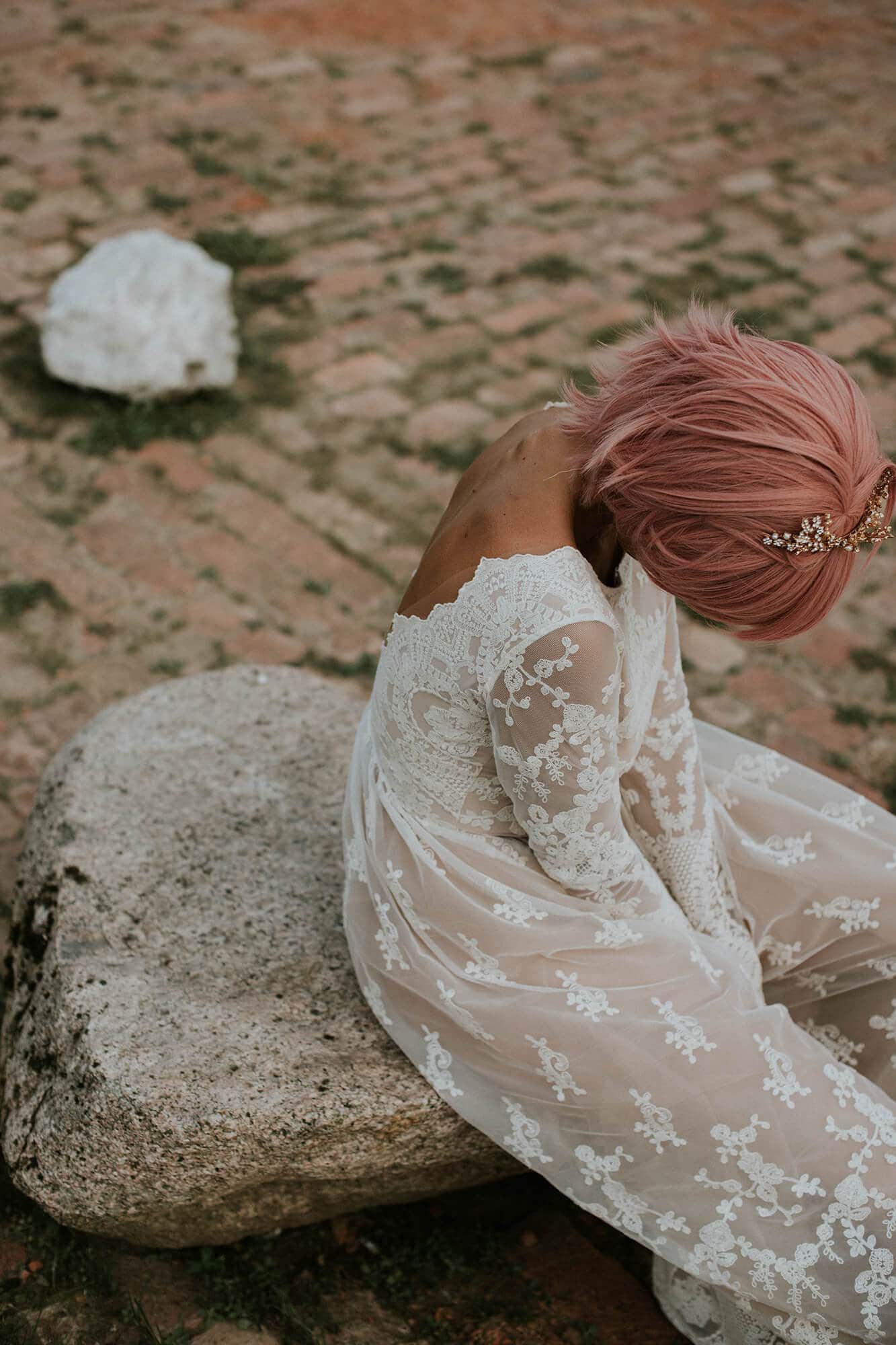 suknia ślubna z długimi rękawami i koronkowymi detalami, osoba siedząca na kamiennej powierzchni