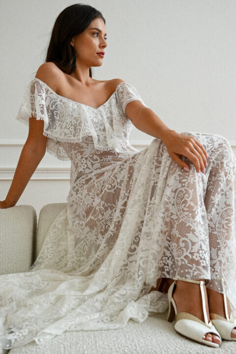 suknia ślubna z koronkowym wykończeniem i odkrytymi ramionami, modelka siedzi na kanapie