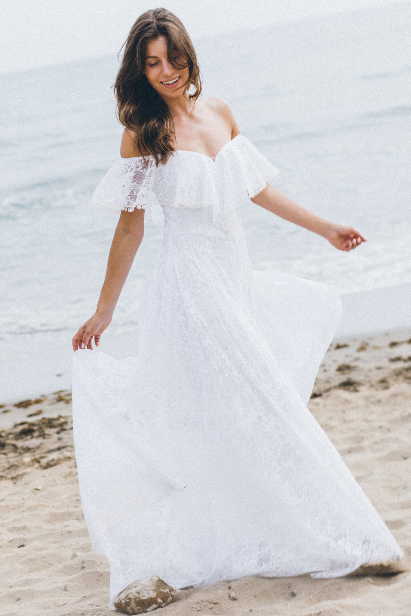 suknia ślubna z odkrytymi ramionami, z koronkowymi detalami, na plaży w pobliżu morza