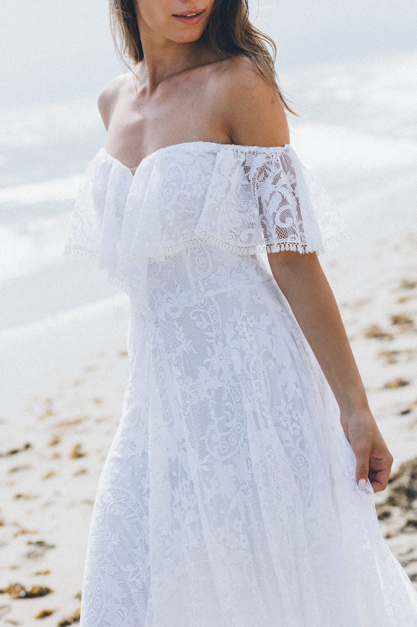 suknia ślubna z koronkowymi rękawami i dekoltem typu off-shoulder, na tle plaży