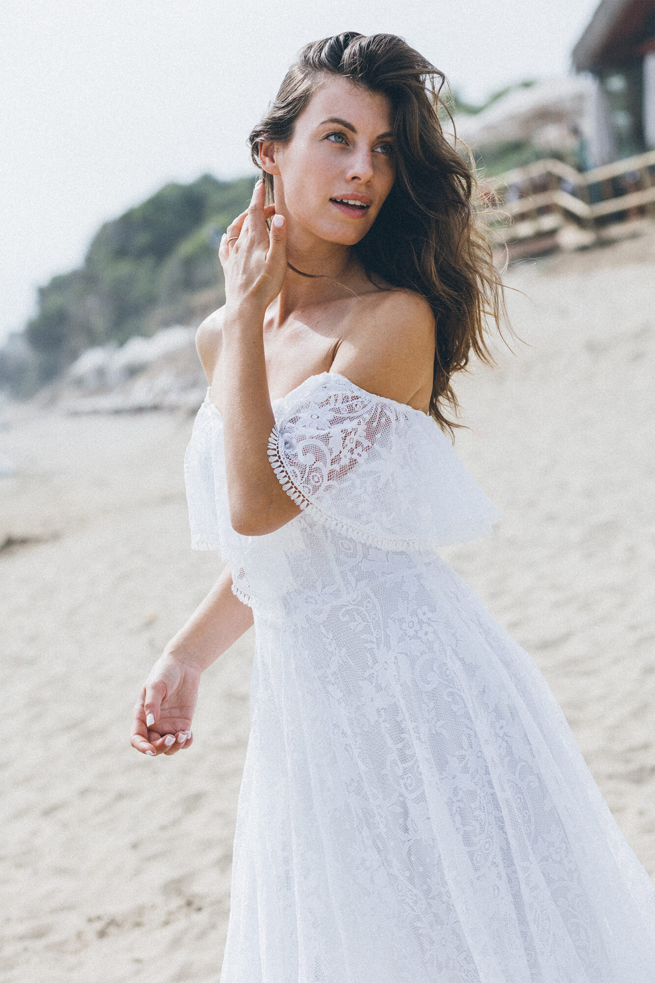suknia ślubna z koronkowymi rękawami, modelka na plaży z delikatnym makijażem i falującymi włosami