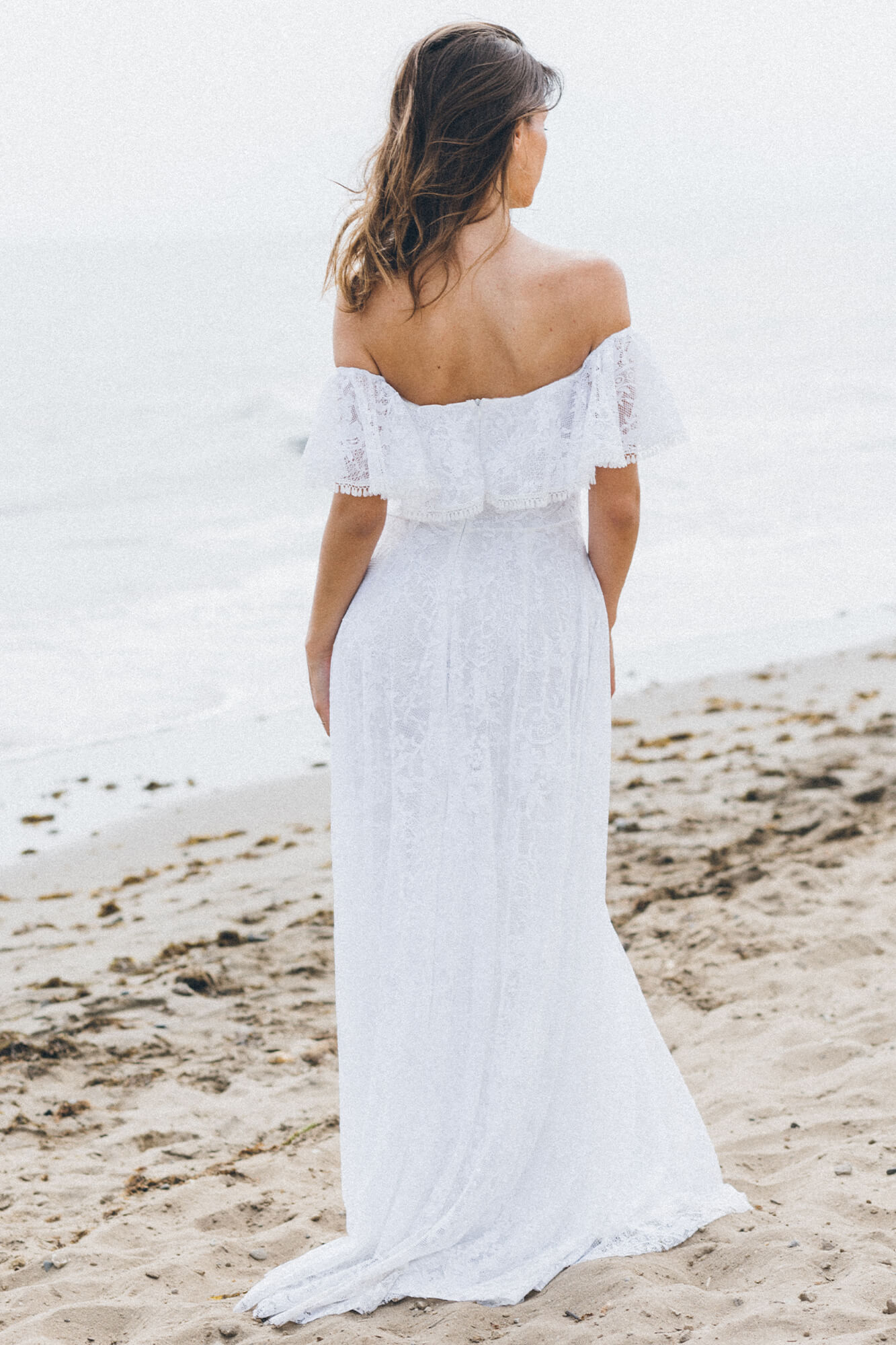 suknia ślubna z odkrytymi ramionami, z koronkowym wykończeniem, widoczna na plaży