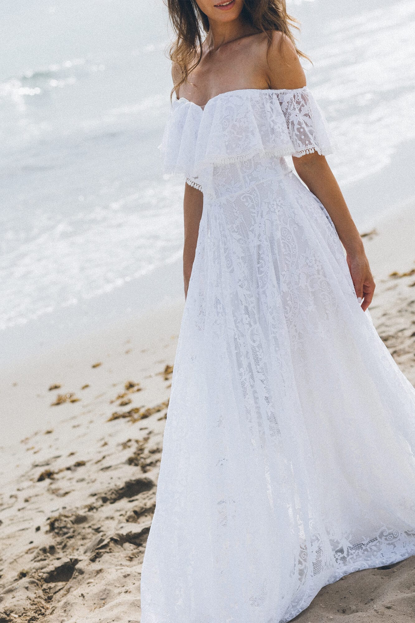 suknia ślubna z odkrytymi ramionami, z koronkowym wykończeniem i długim dołem na plaży