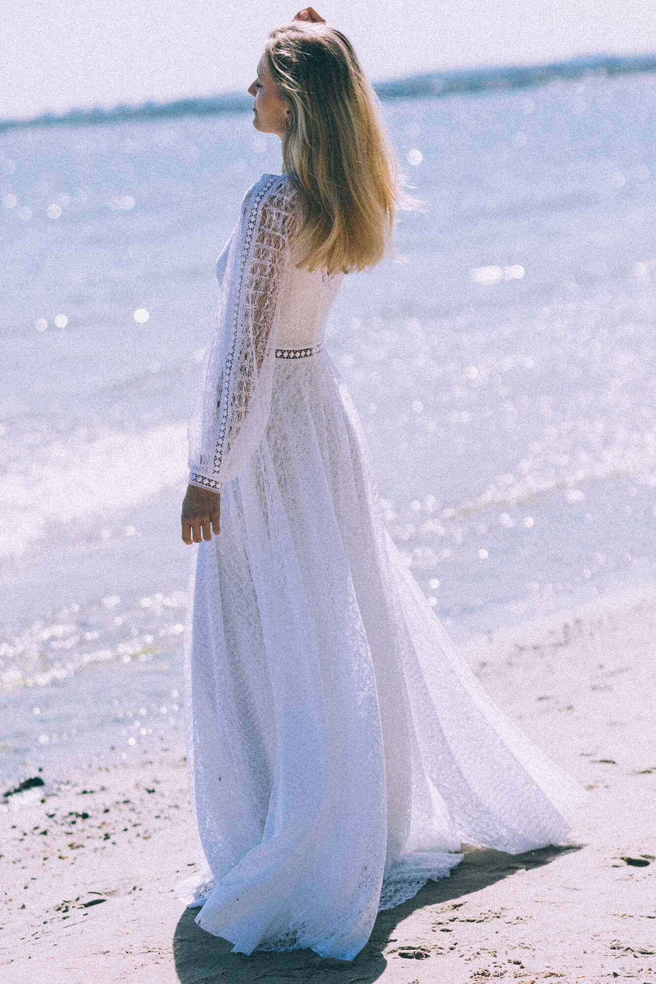 suknia ślubna z długimi rękawami, biała, z delikatnym materiałem, na tle plaży i morza