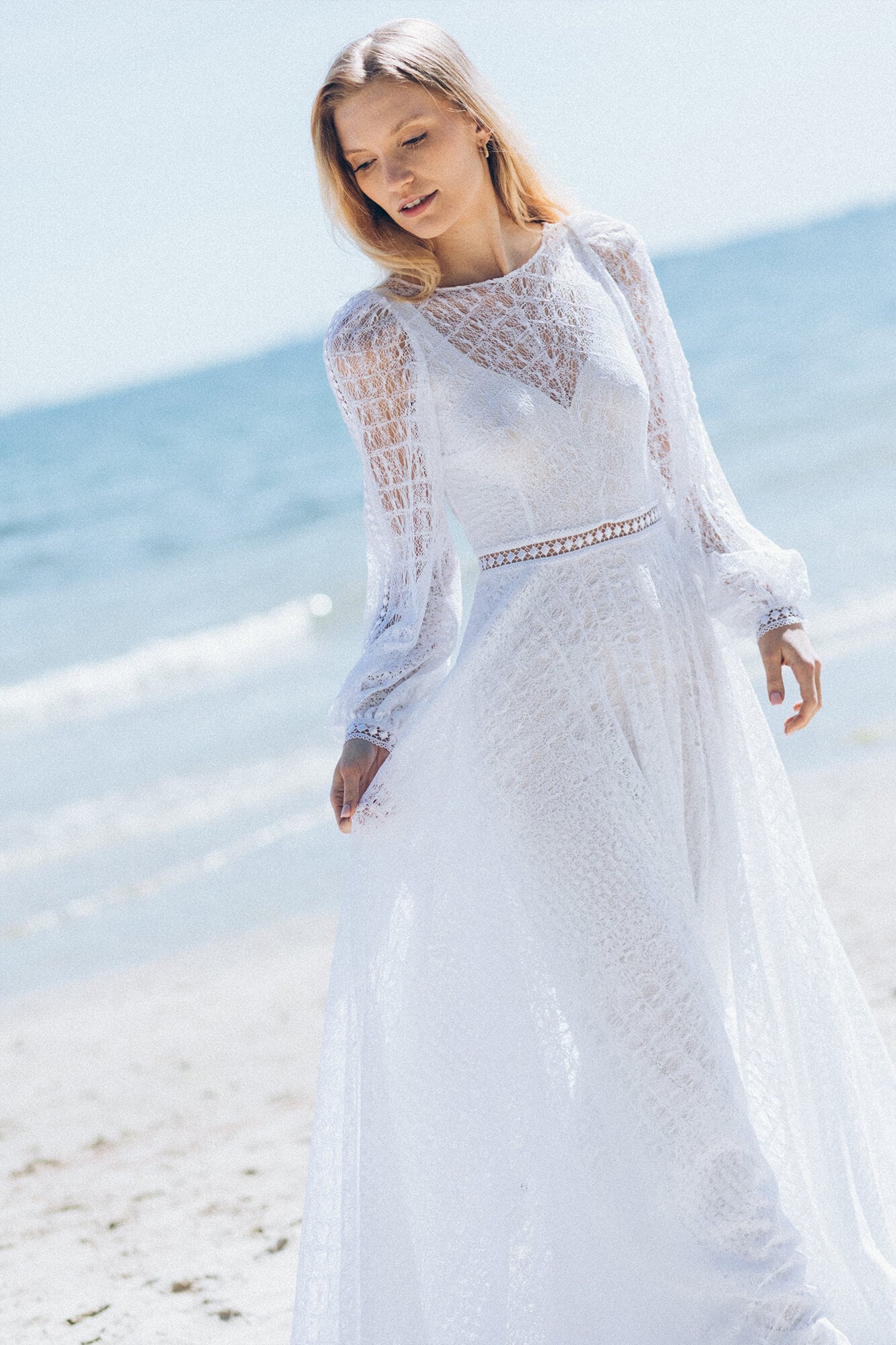 suknia ślubna z długimi koronkowymi rękawami, z lekkiego materiału, na tle plaży i morza