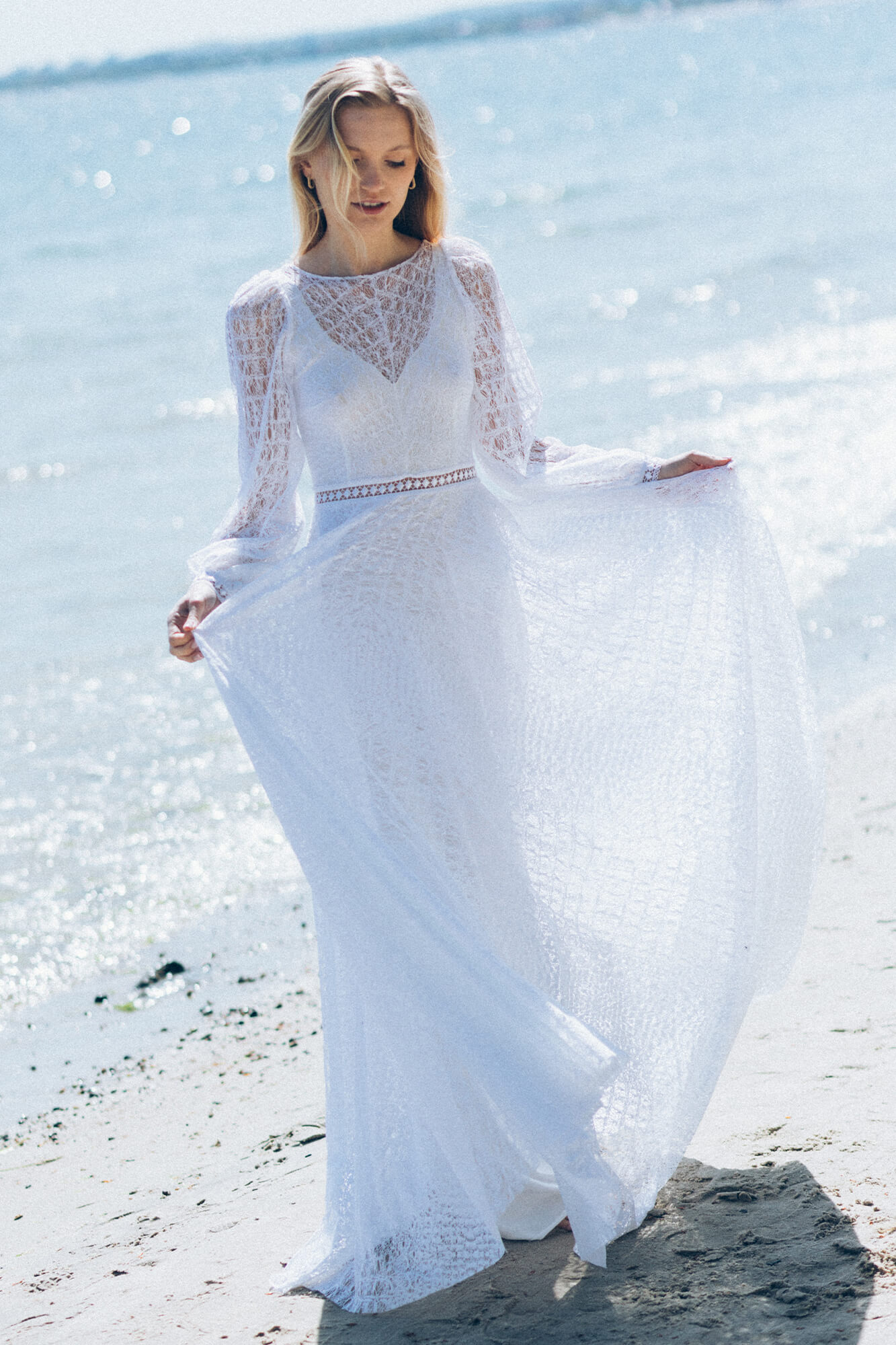 suknia ślubna z długimi rękawami i koronkowym dekoltem, uniesiona na wietrze nad brzegiem morza