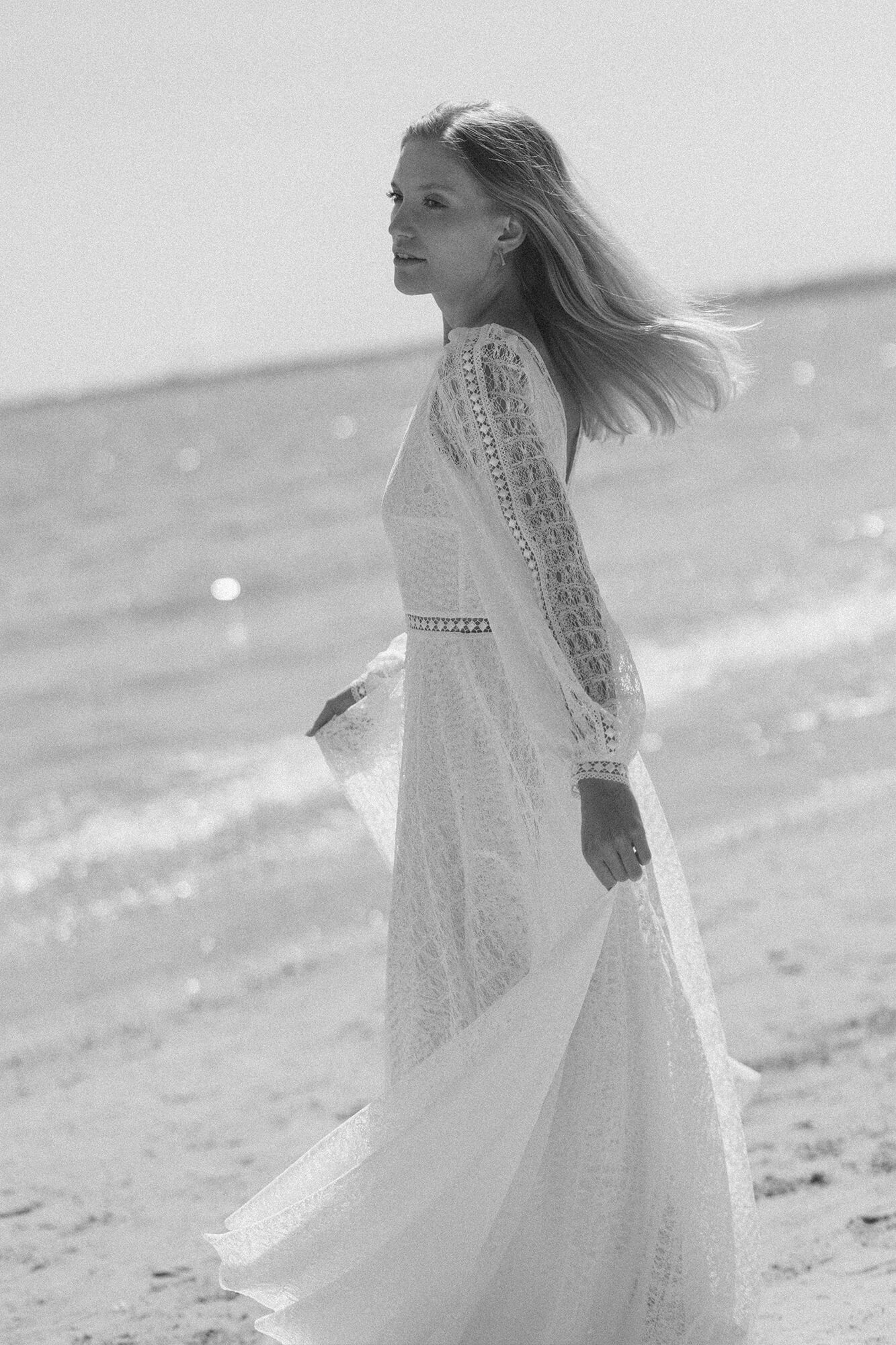 suknia ślubna z długimi koronkowymi rękawami, biała, noszona przez kobietę na plaży