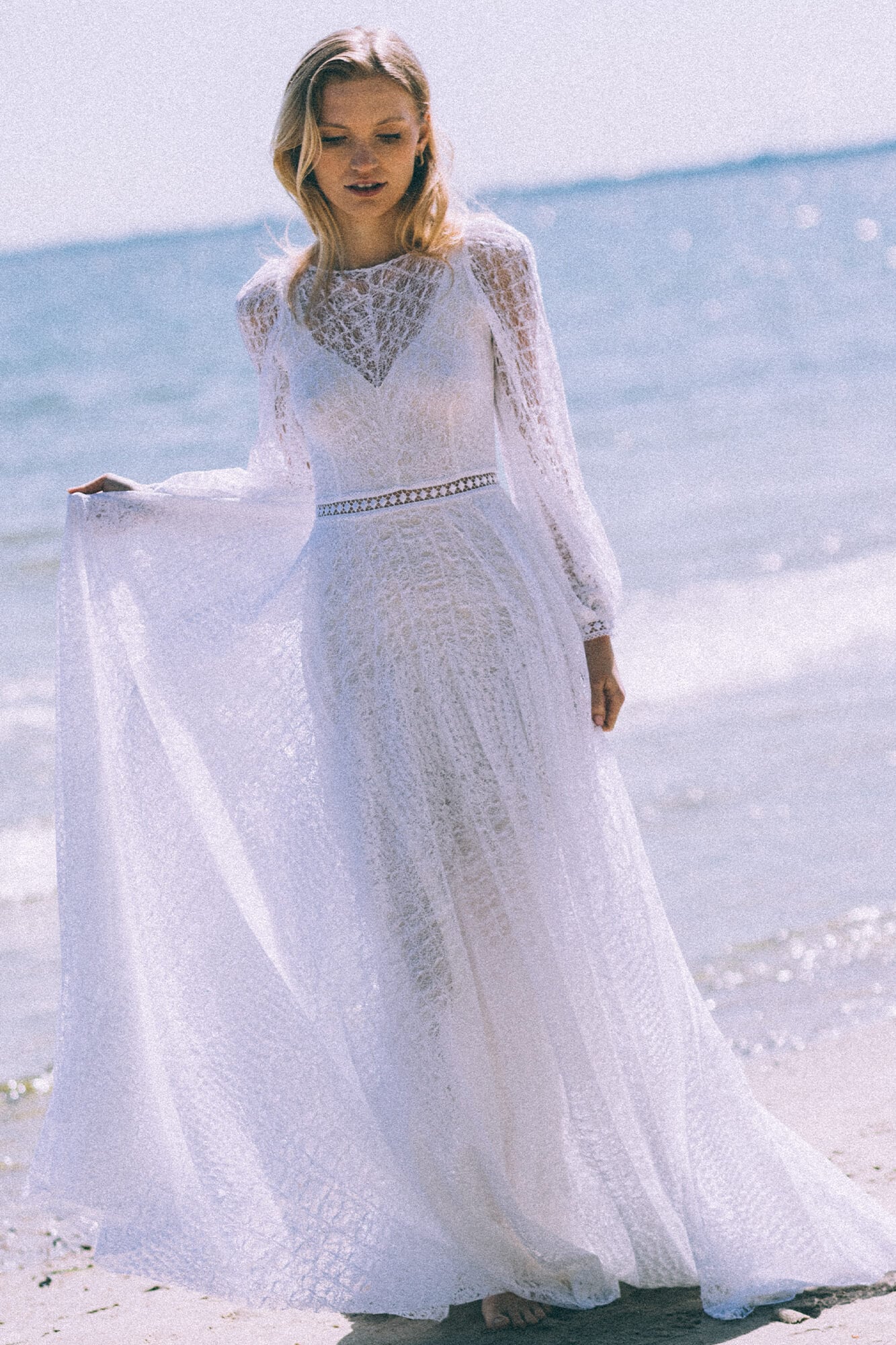 suknia ślubna z długimi rękawami, koronkowym dekoltem i trenem, na tle morza