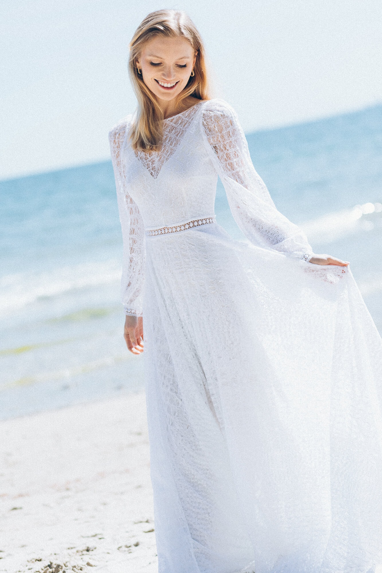 suknia ślubna z długimi rękawami, wykonana z białego materiału, stojąca na plaży przy morzu