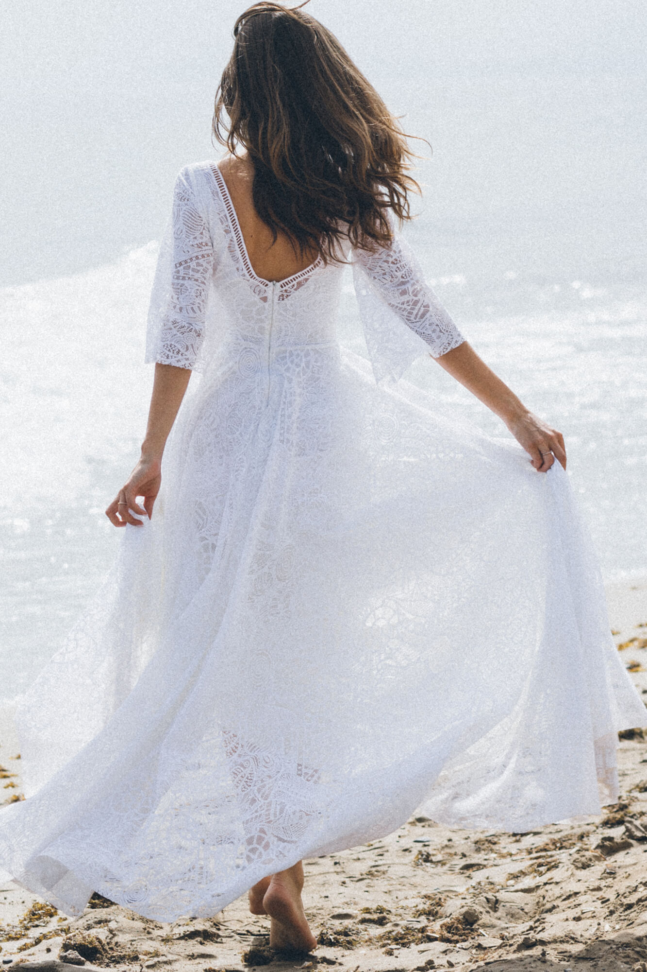 suknia ślubna z długimi rękawami, z koronkowymi detalami, widoczna na tle morza.