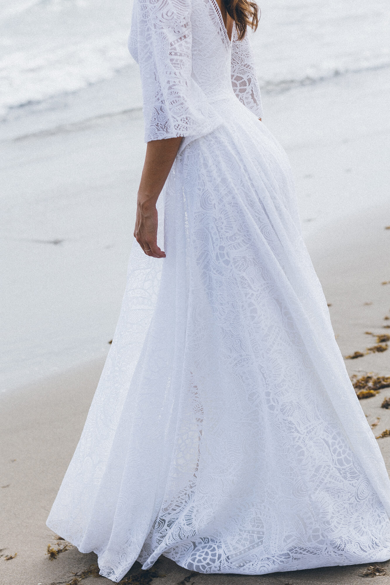 suknia ślubna z długim rękawem, zdobiona koronką, w kolorze białym, na tle plaży.