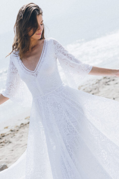 suknia ślubna z długimi koronkowymi rękawami i dekoltem w serek, prezentująca się na plaży