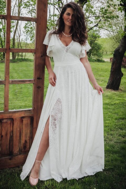 Suknia ślubna z koronkowymi rękawami, z dekoltem w kształcie litery V i rozcięciem z przodu.
