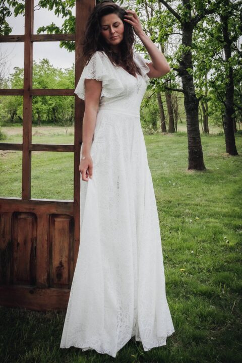 Suknia ślubna z krótkimi, falbaniastymi rękawami, wykonana z białego materiału w delikatny wzór.