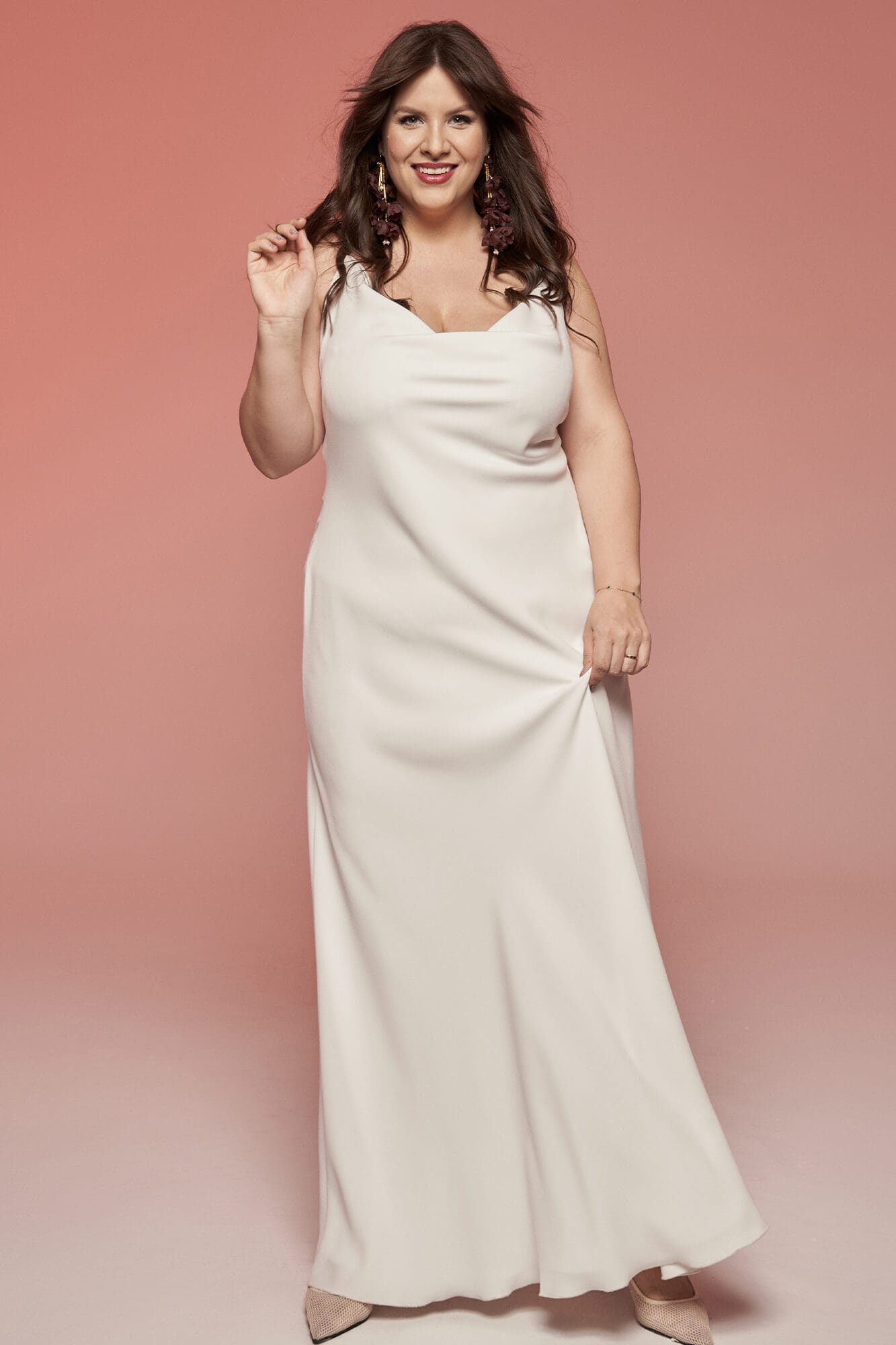 suknia ślubna w kolorze białym, z dekoltem i luźnym krojem, modelka trzyma rękę w górze.