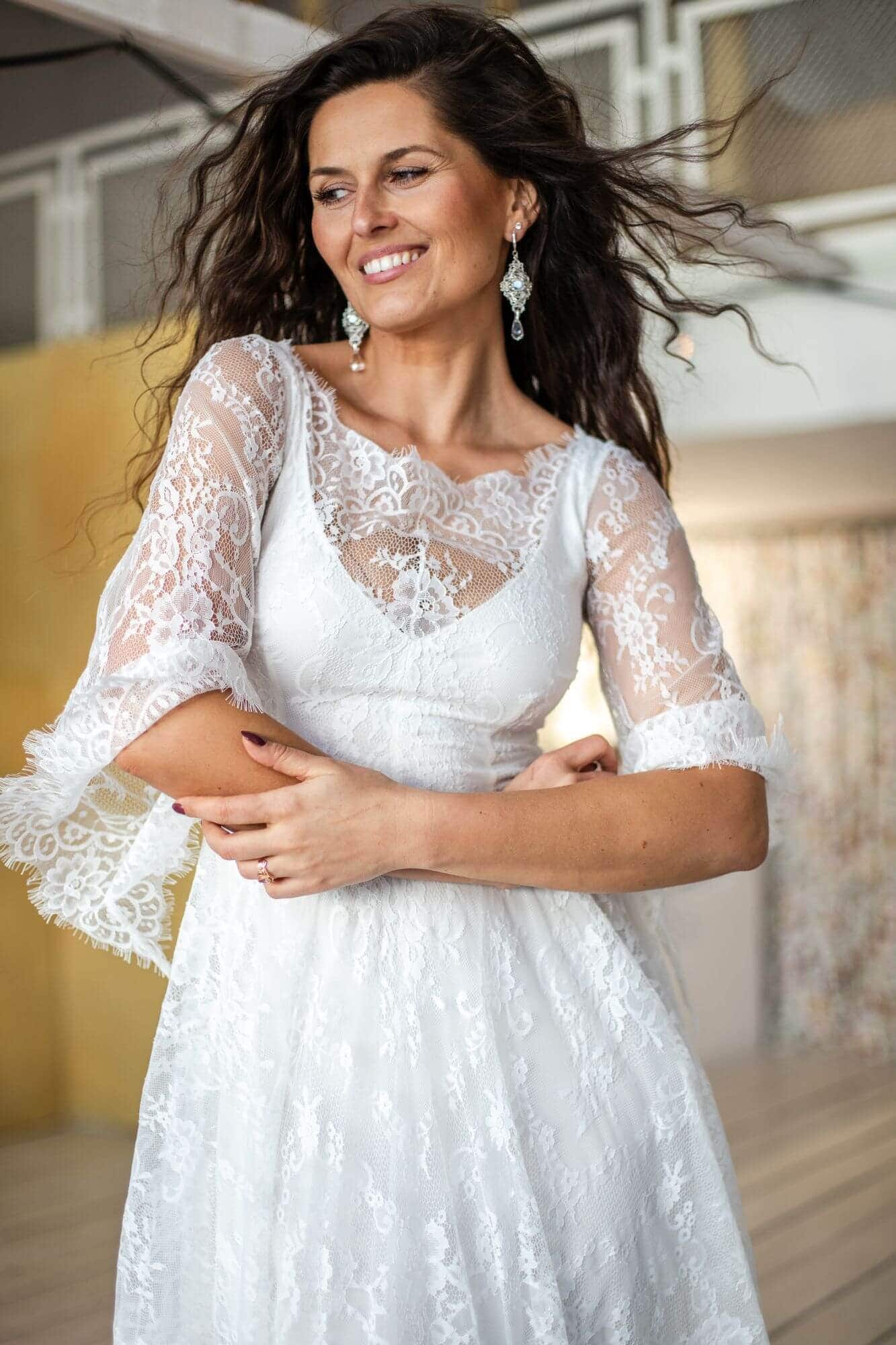 suknia ślubna z koronkowymi rękawami i falbanami, modelka w ruchu, uśmiechnięta, z długimi włosami