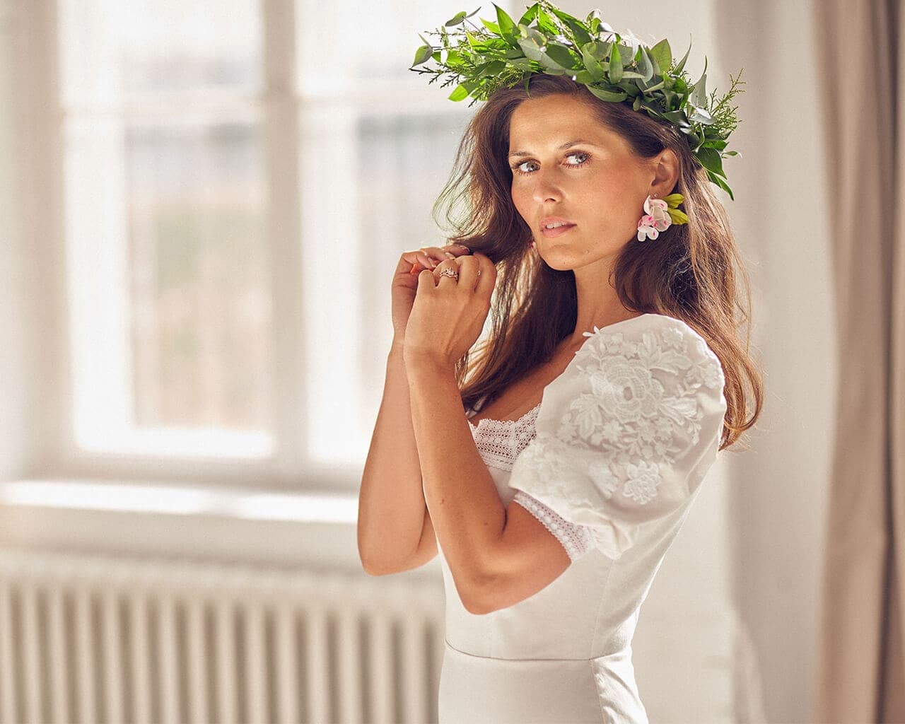 Kobieta w sukni ślubnej z koronkowymi rękawami, nosząca wianek z zieleni.