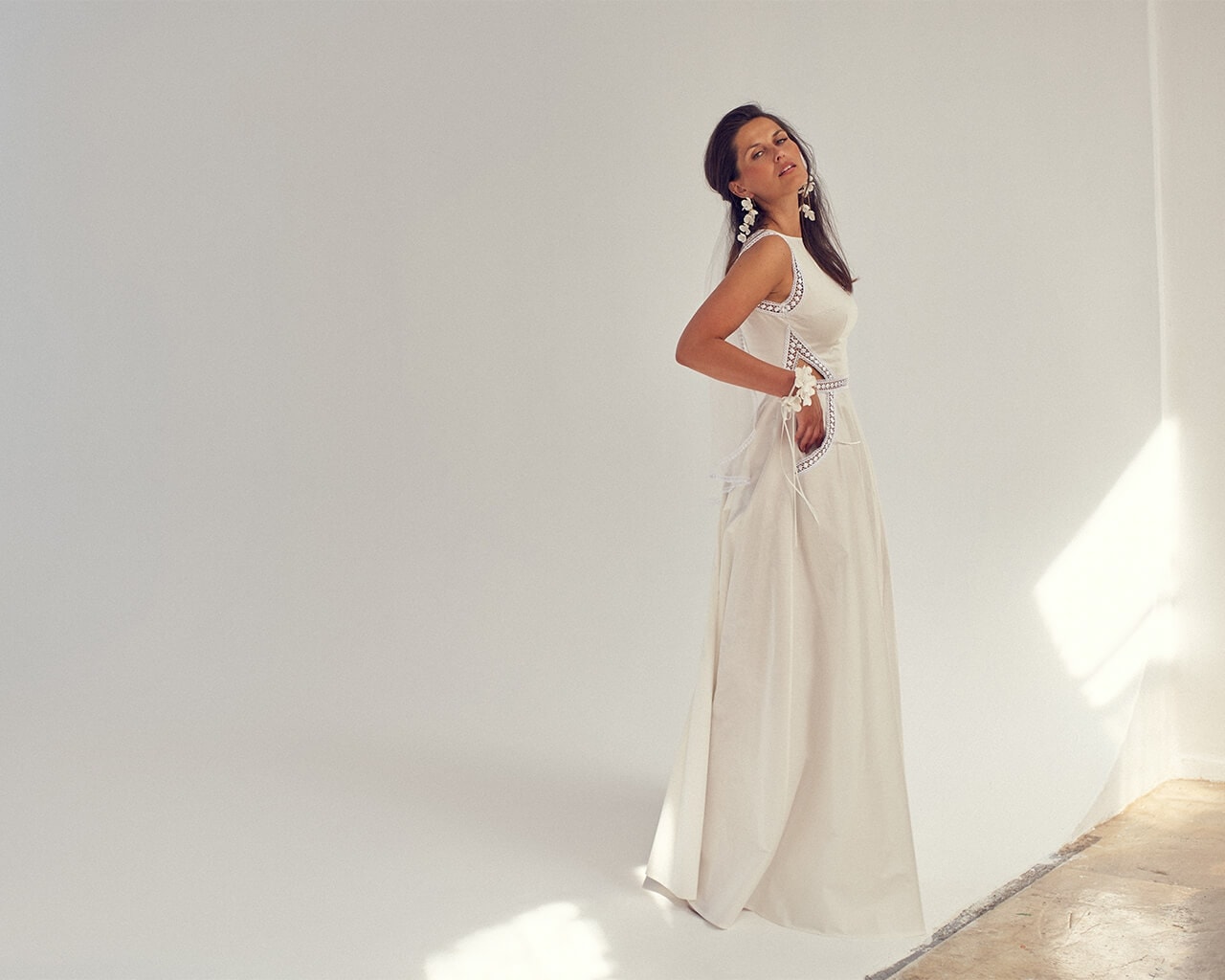 suknia ślubna w kolorze białym, z odkrytymi ramionami i długim dołem, prezentowana przez kobietę na neutralnym tle