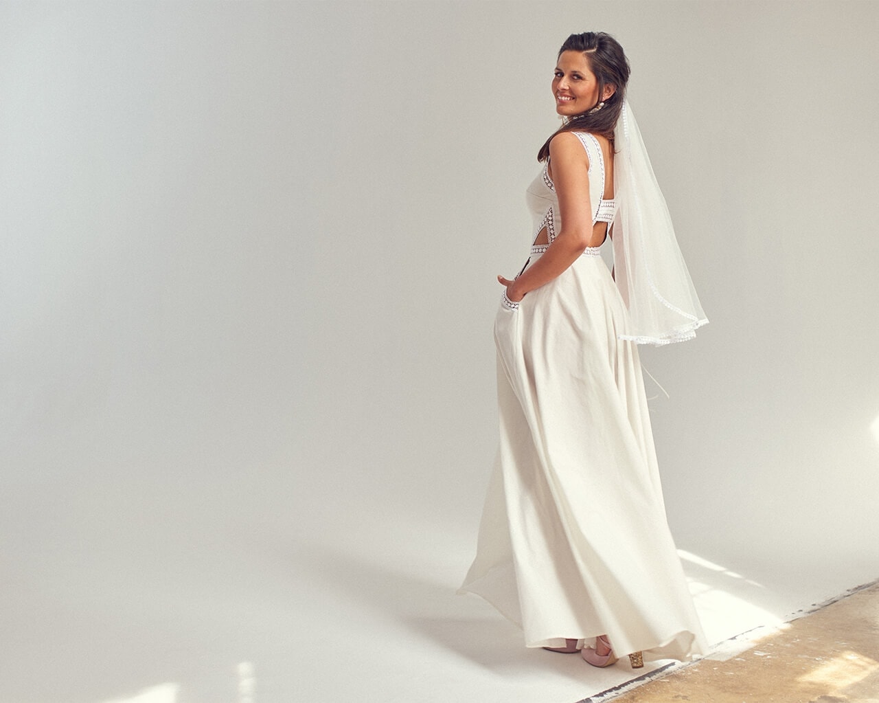 suknia ślubna z długim welonem, modelka stoi na tle szarej ściany