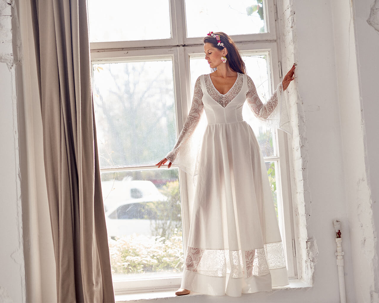 suknia ślubna z długimi rękawami, stojąca przy oknie w jasnym pomieszczeniu