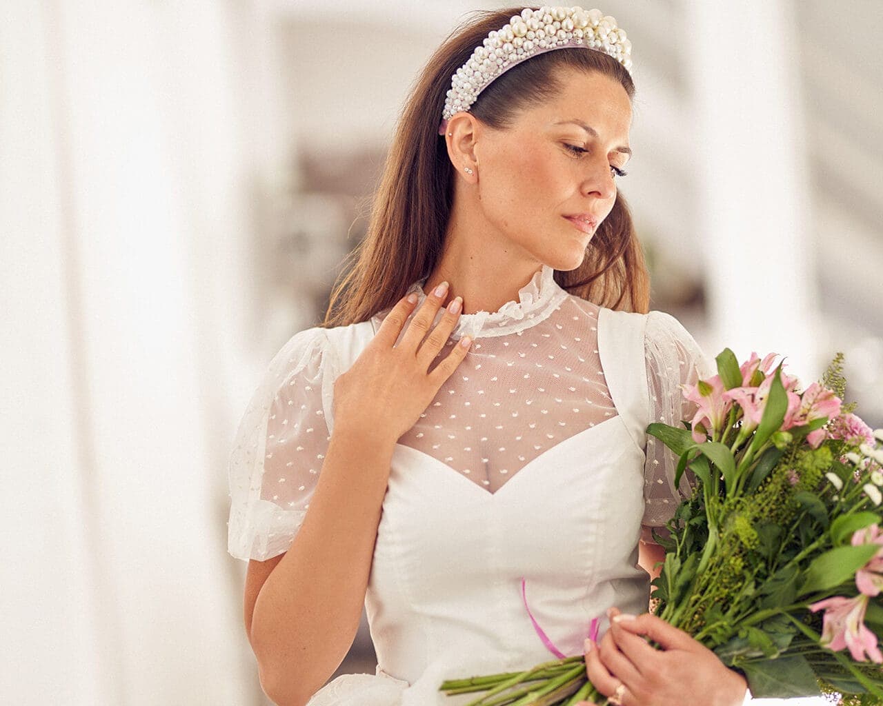 suknia ślubna z koronkowym dekoltem i bufkami, trzymana przez kobietę z bukietem kwiatów