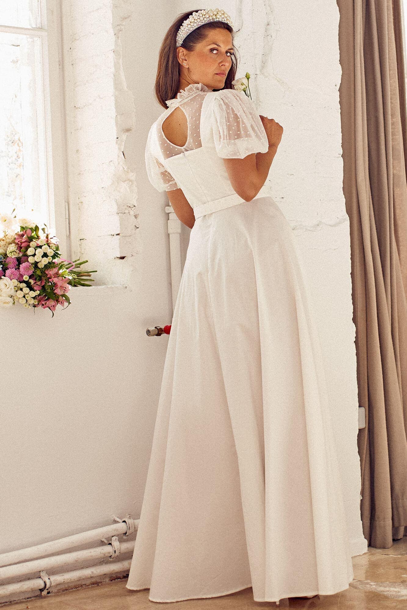 suknia ślubna z krótkimi rękawami i długim dołem, widoczna z tyłu przy oknie.