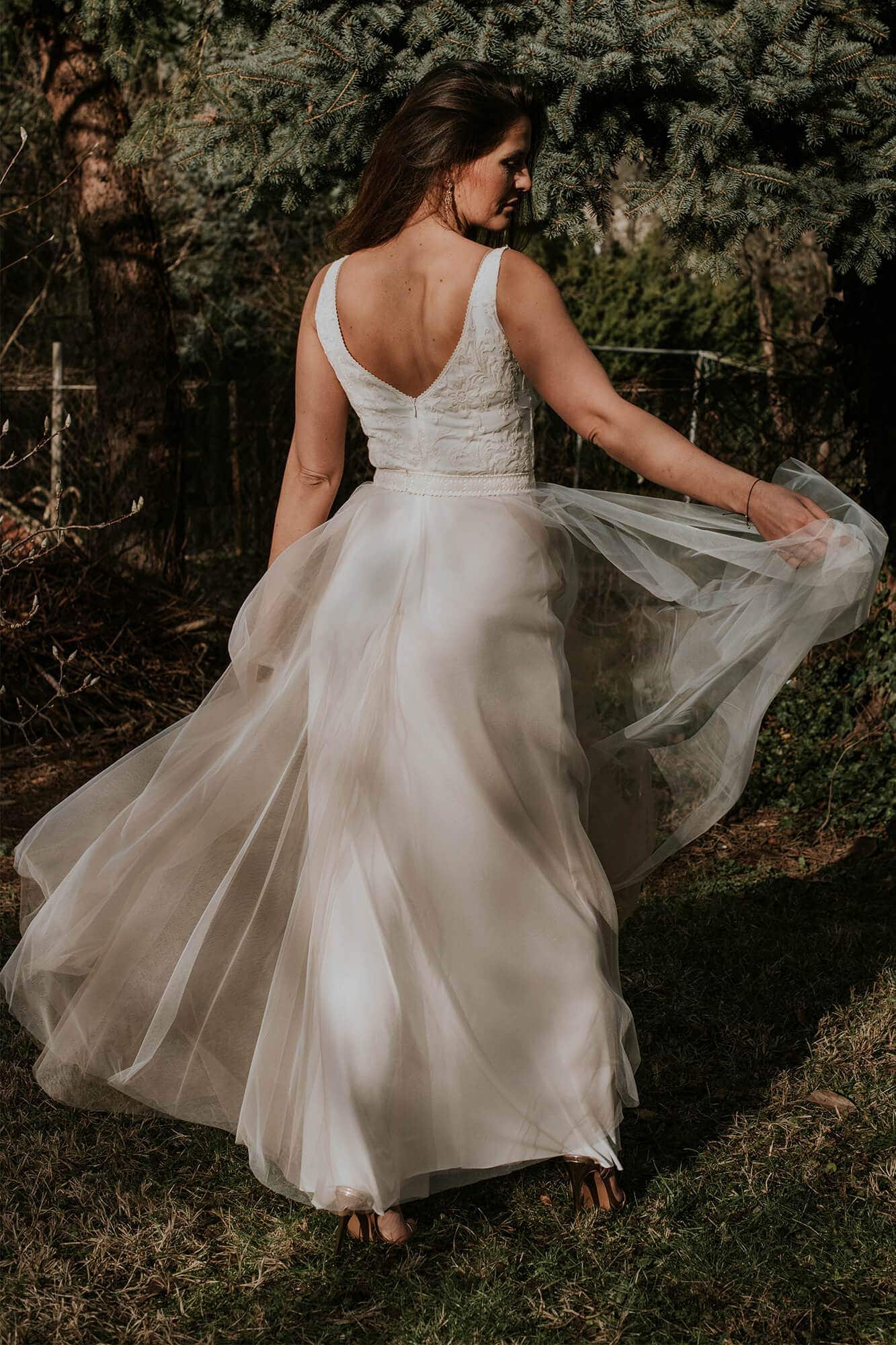 suknia ślubna z odkrytymi plecami i zwiewnym dołem, widoczna z tyłu w otoczeniu zieleni