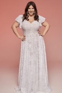 suknia ślubna z koronkowym wykończeniem i rękawami, w kolorze białym, na modelce w neutralnym tle