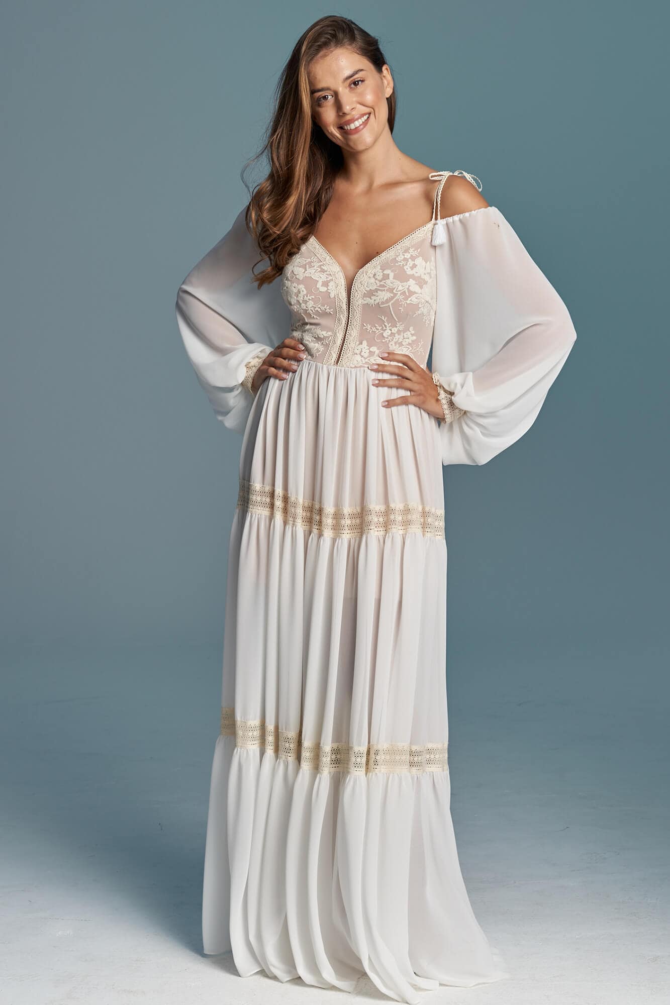 Suknia ślubna z długimi rękawami, ozdobiona koronkowym detalem i złotymi akcentami.