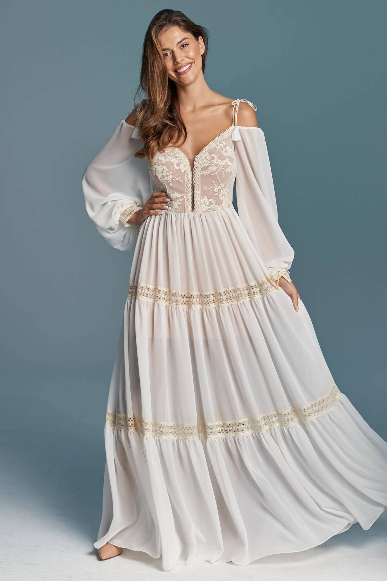 suknia ślubna z długimi rękawami, dekoltem w kształcie litery V i złotymi detalami.