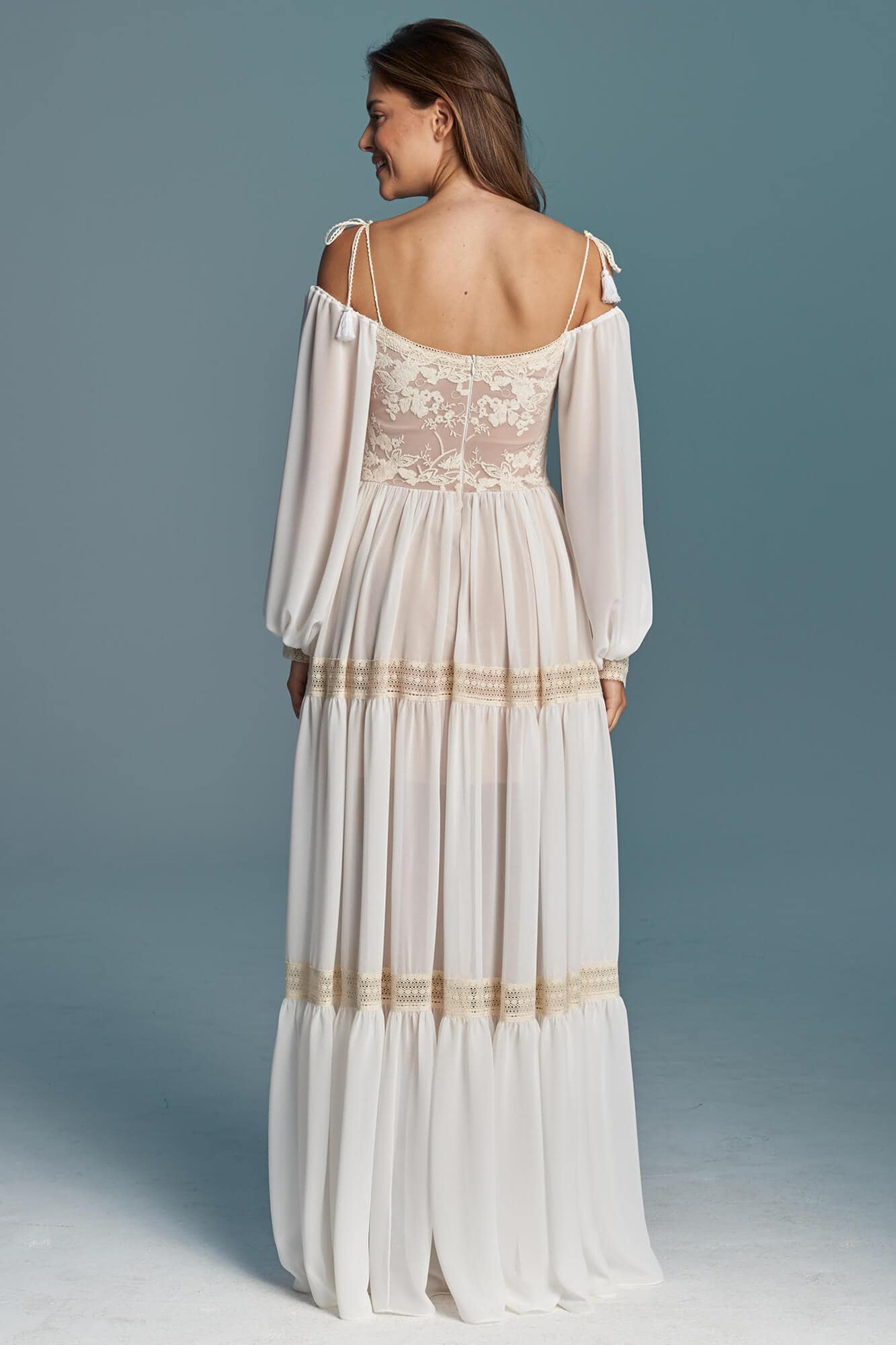 suknia ślubna z długimi rękawami, odkrytymi plecami i falbanami u dołu.