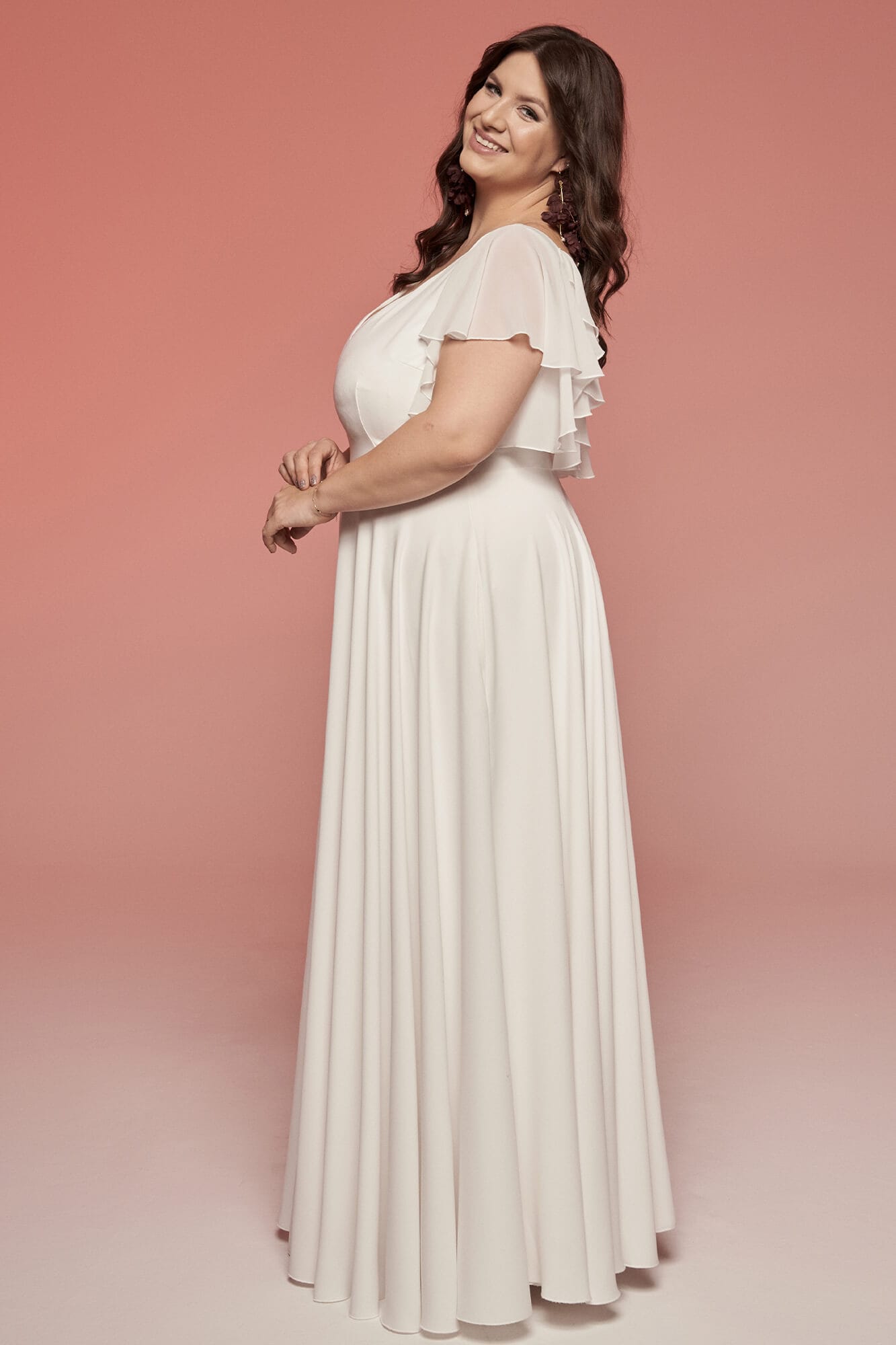 suknia w kolorze białym z krótkimi rękawami, o luźnym kroju, prezentująca się na kobiecie w profilu