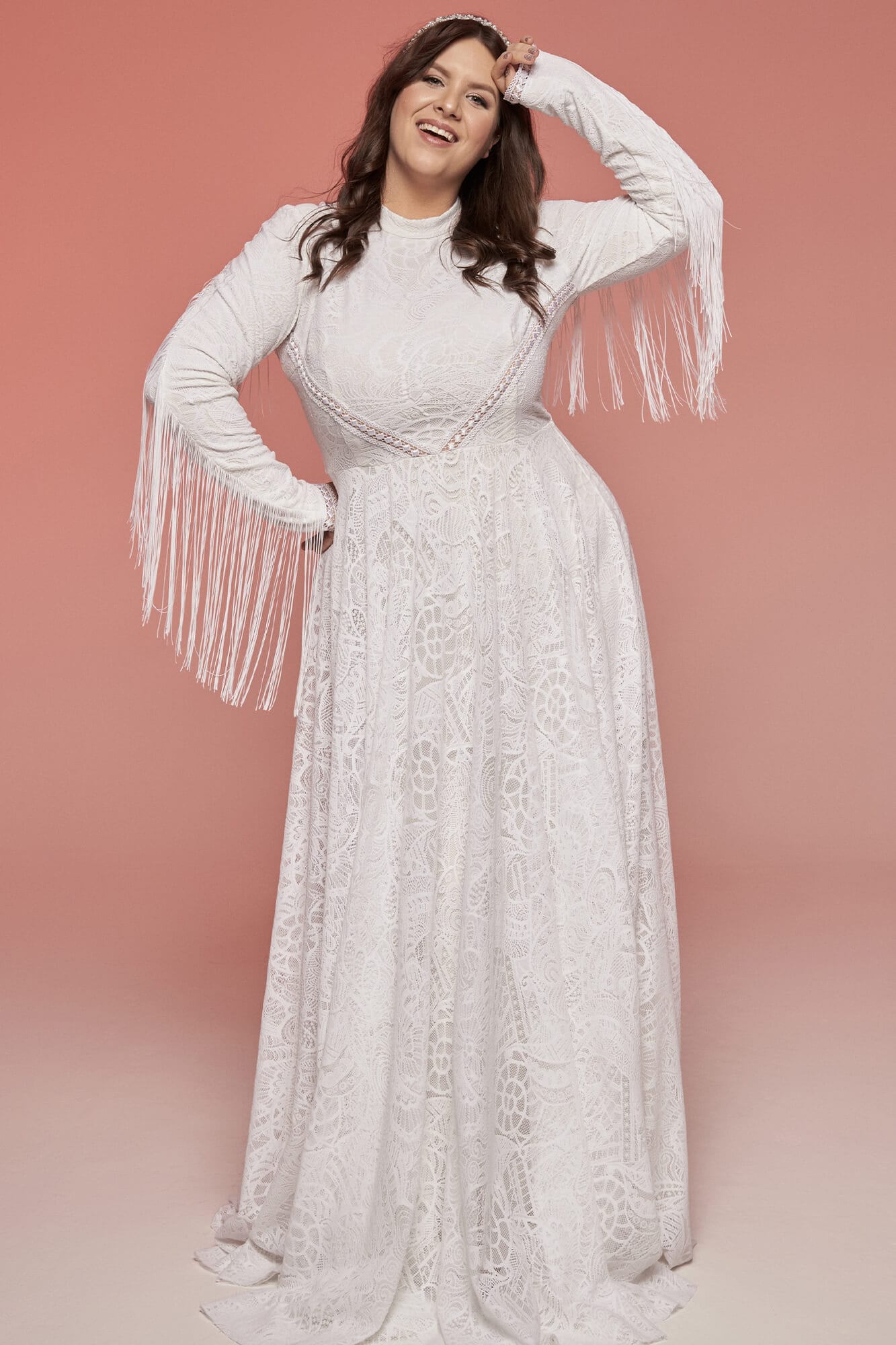 suknia ślubna z długimi rękawami, koronkowym materiałem i frędzlami na mankietach, na tle różowym